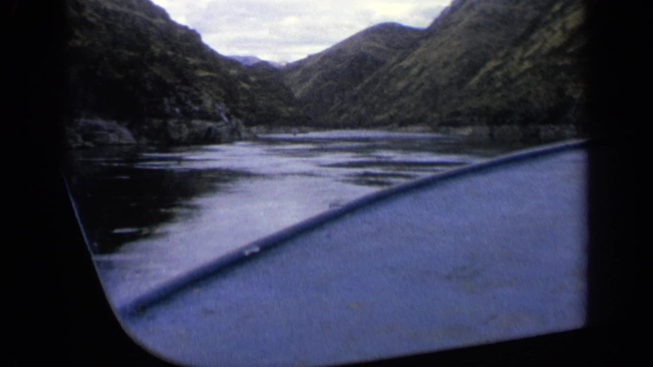 Boat bow moving through a narrow mountain river under an overcast sky.