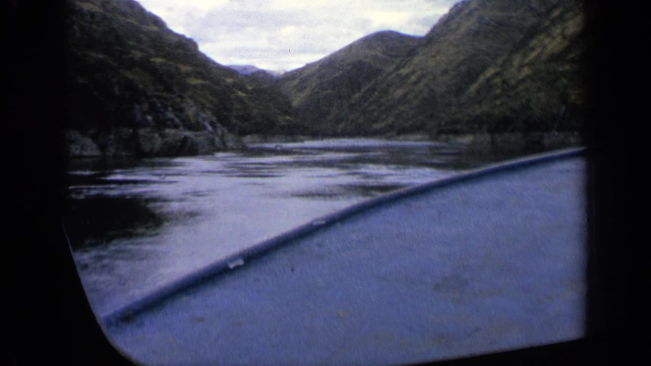 Boat bow cuts across reflective water in a narrow valley river.