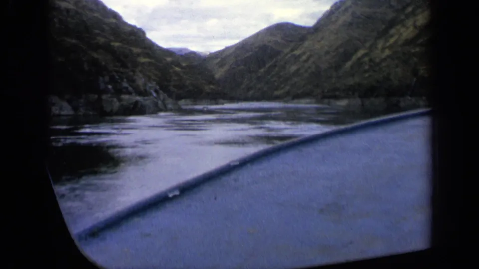 First-person boating view on an Idaho mountain river, with reflective water and forested slopes visible ahead.