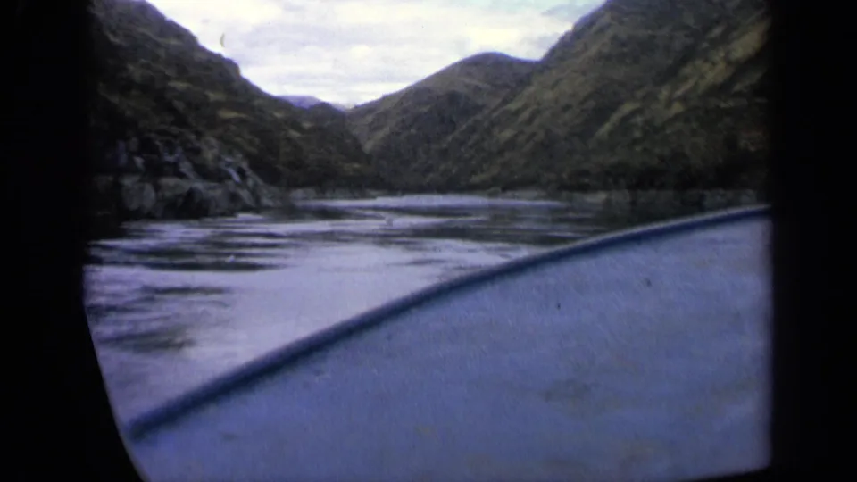 Vintage 8mm Idaho boating frame with the bow at lower right and a narrow mountain river stretching ahead.