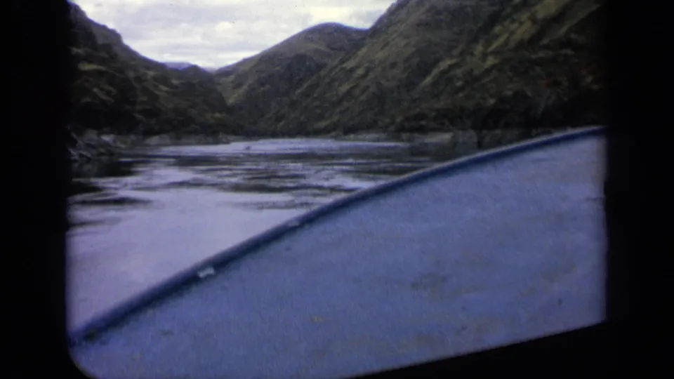 1963 Idaho home-movie view over a boat edge toward a narrow calm river passage between steep mountain slopes.