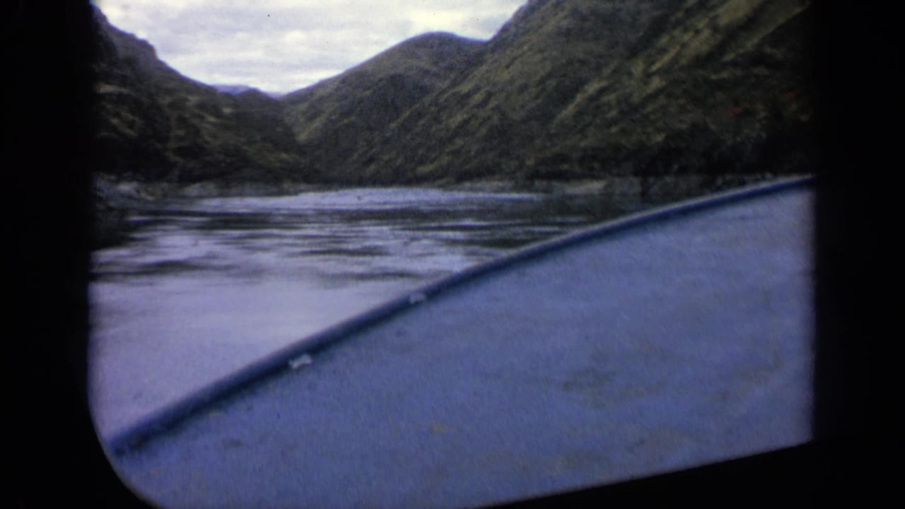 Boat edge in the foreground on a calm river between steep green hills.