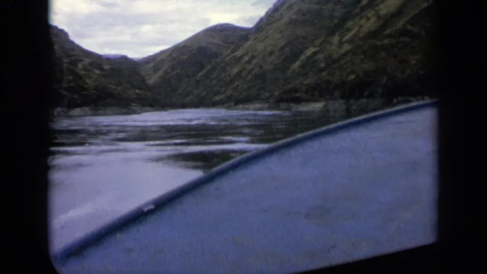 Low-angle 8mm boat view on a calm Idaho river, showing wooded hillsides and a narrow valley ahead.