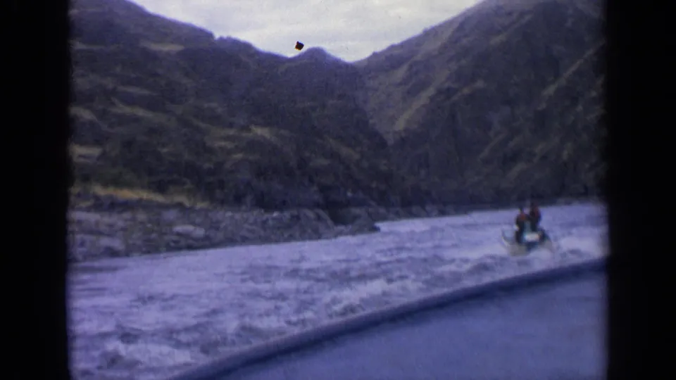 Wide 8mm view of a rider on a small motorized craft traveling along an Idaho waterway framed by steep hills.