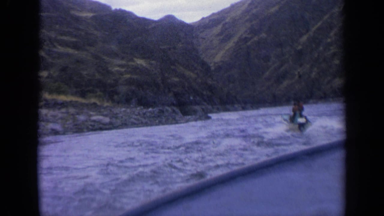 1963 Idaho 8mm frame showing a small motorboat moving through rough river water in a steep mountain valley.