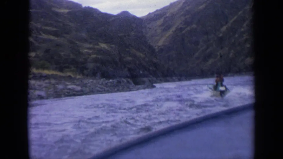 1963 Idaho 8mm frame showing a small motorboat moving through rough river water in a steep mountain valley.