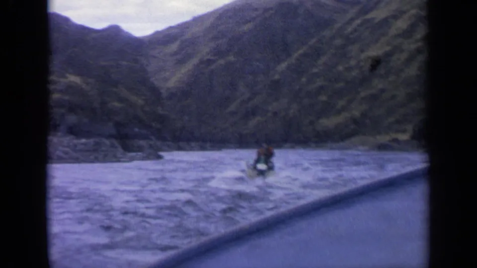 A small motorboat appears ahead on a gray-blue mountain river in archival 8mm footage from Idaho.