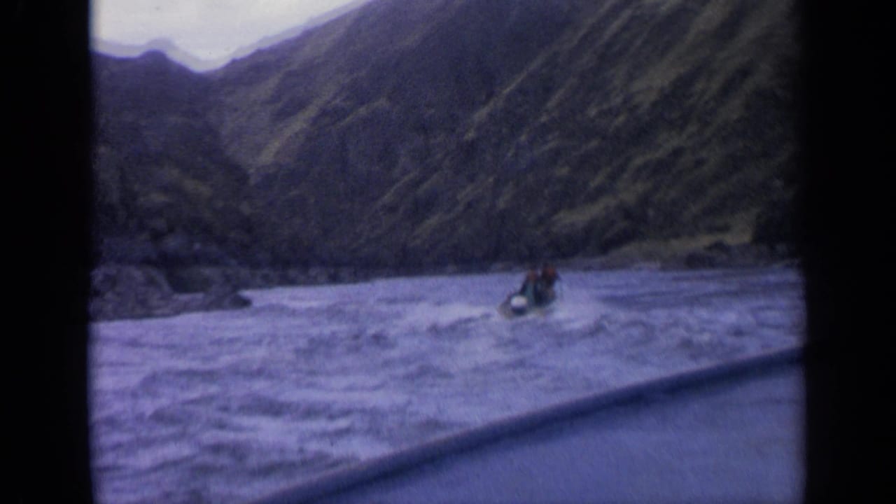 1963 Idaho home-movie frame showing a small motorboat moving across choppy lake water below steep rocky hillsides.