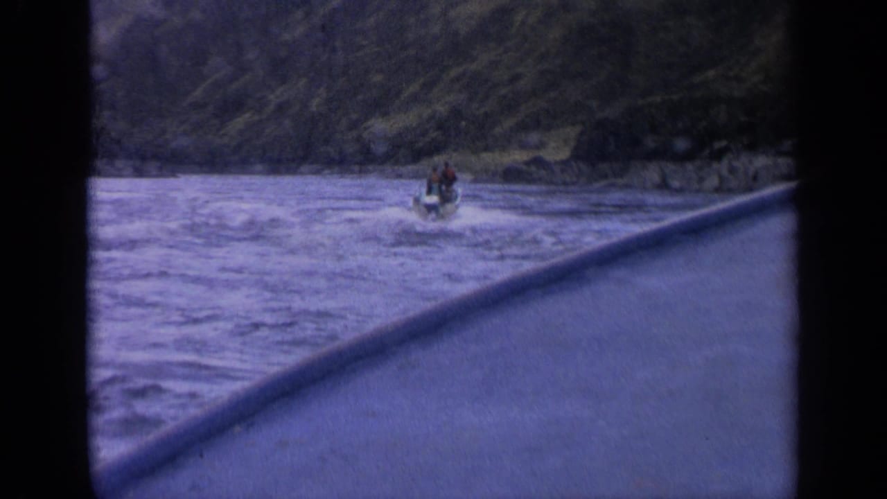 Distant motorboat on an Idaho mountain lake, seen from another moving boat with a blurred foreground rail or hull edge.