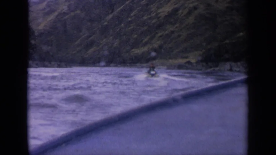End frame of a distant motorboat leaving wake on a mountain lake in Idaho, with steep hills and projector-frame edges visible.