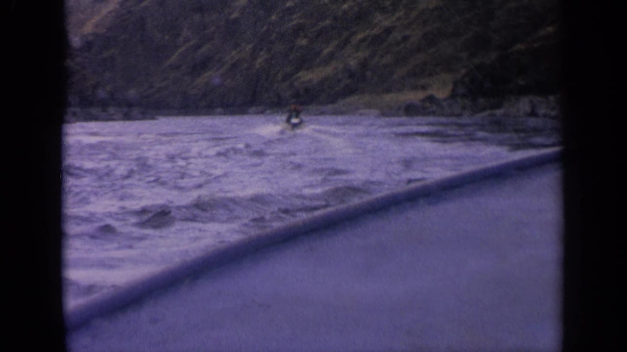 Distant boat continues along choppy river water beside a steep canyon wall.