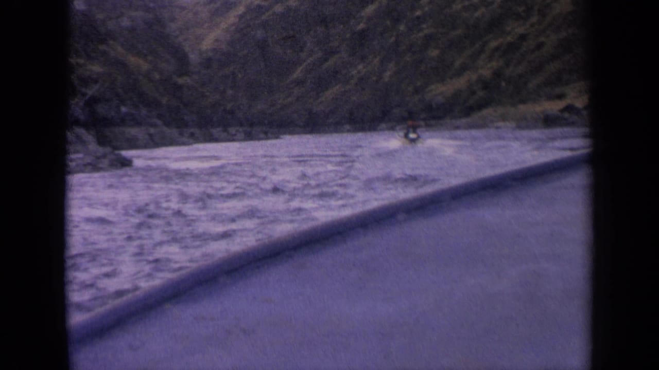 1963 Idaho 8mm frame showing a distant boat moving through fast water in a mountain river canyon.