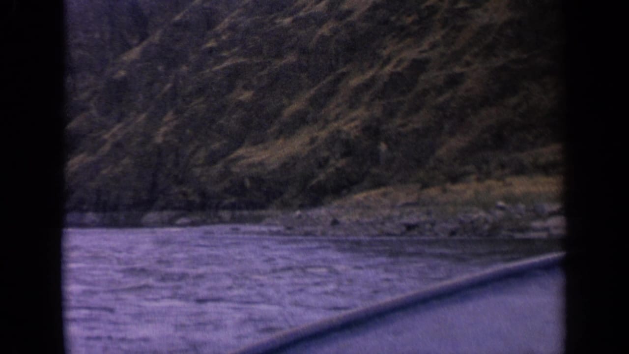 1963 Idaho 8mm frame of rushing river water and steep canyon hillside, with a diagonal foreground edge.