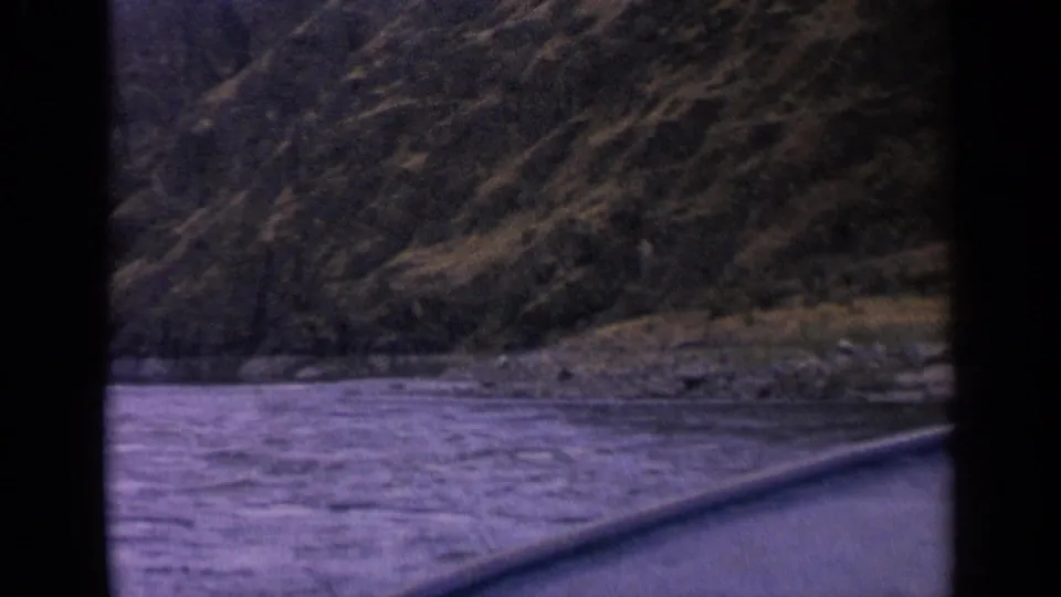 1963 Idaho 8mm frame of rushing river water and steep canyon hillside, with a diagonal foreground edge.