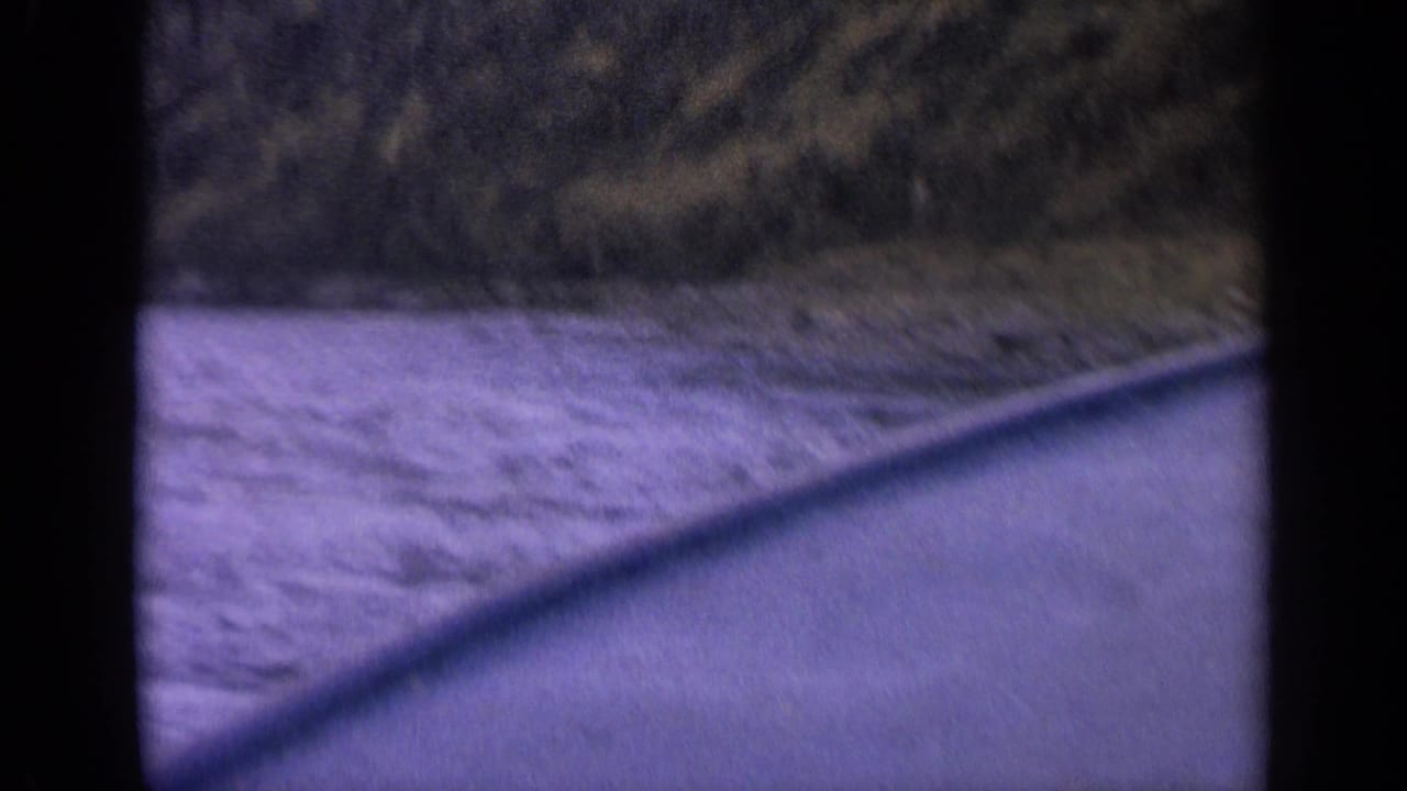 Soft, motion-blurred 1963 Idaho 8mm frame showing river water, a boat edge, and a rocky mountain shoreline.