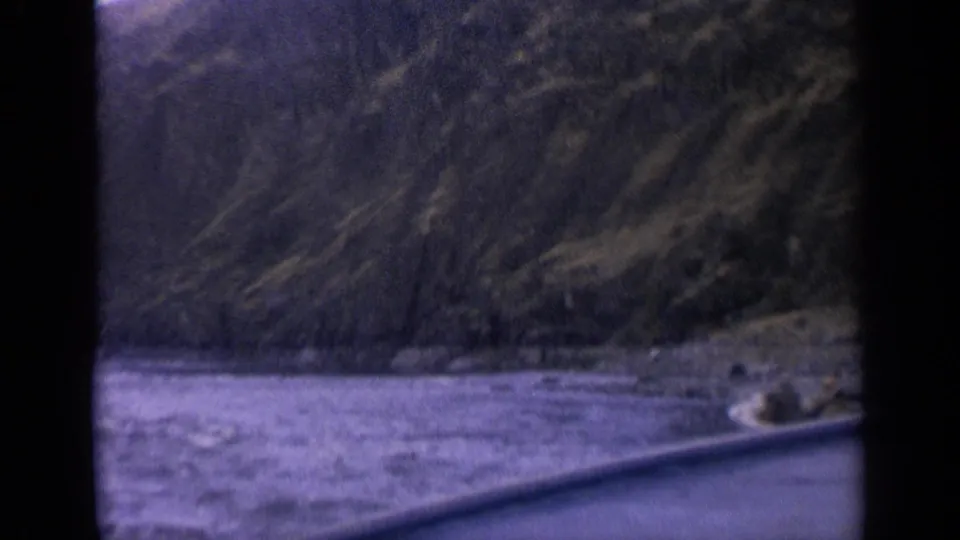 1963 Idaho 8mm home-movie frame showing choppy water, rugged shoreline, and a small boat entering view behind dark frame edges.