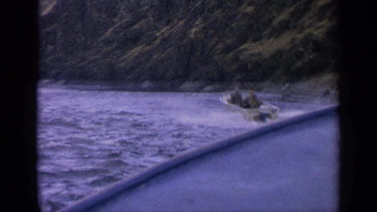 Small speedboat crosses choppy blue water with white spray in front of a steep mountain shore.