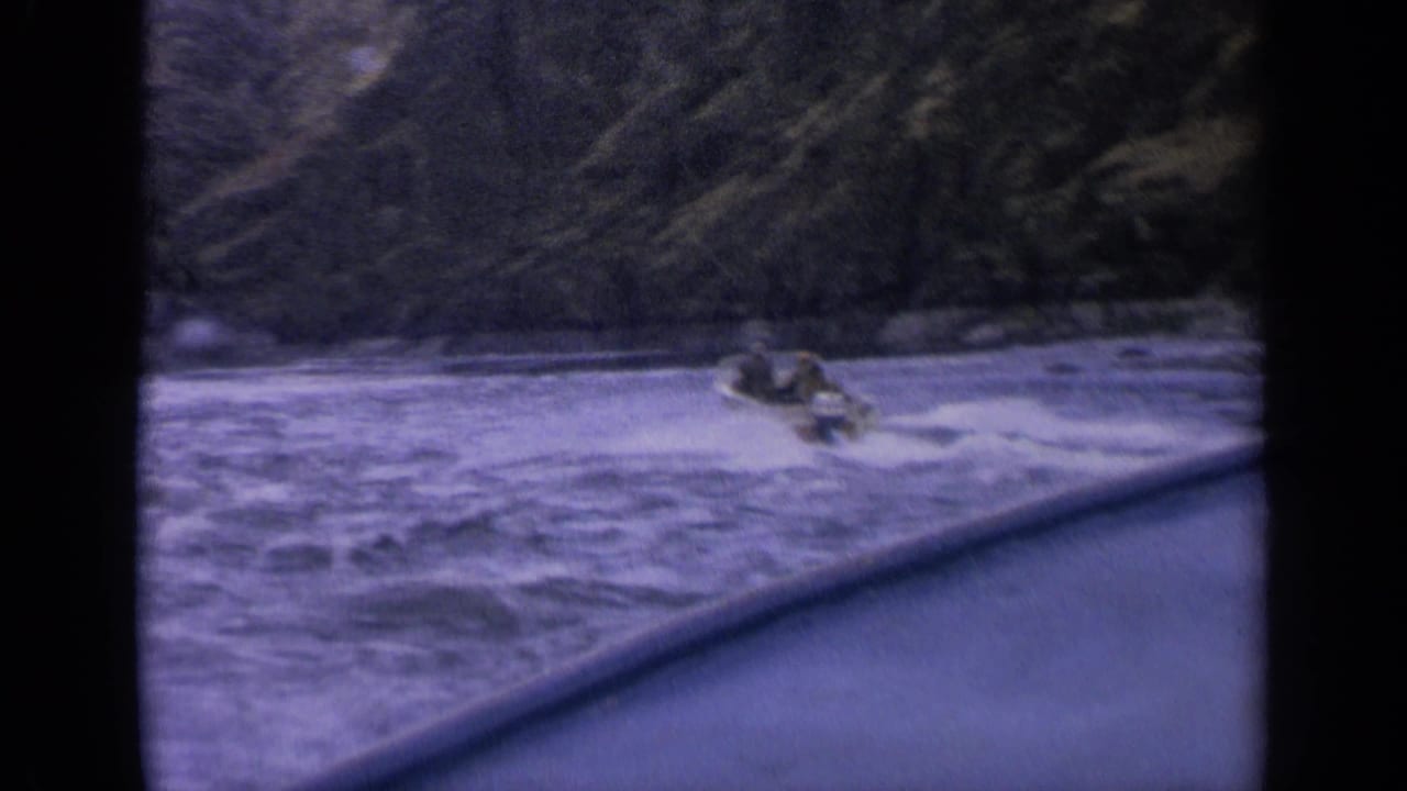 1963 Idaho 8mm frame showing a small speedboat and faint occupants speeding over rough water, filmed from behind a dark foreground edge.