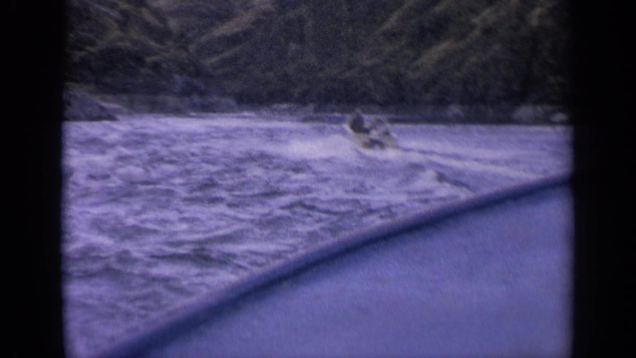 1963 Idaho 8mm home-movie frame of a small speedboat receding over choppy water against a wooded mountain shoreline.