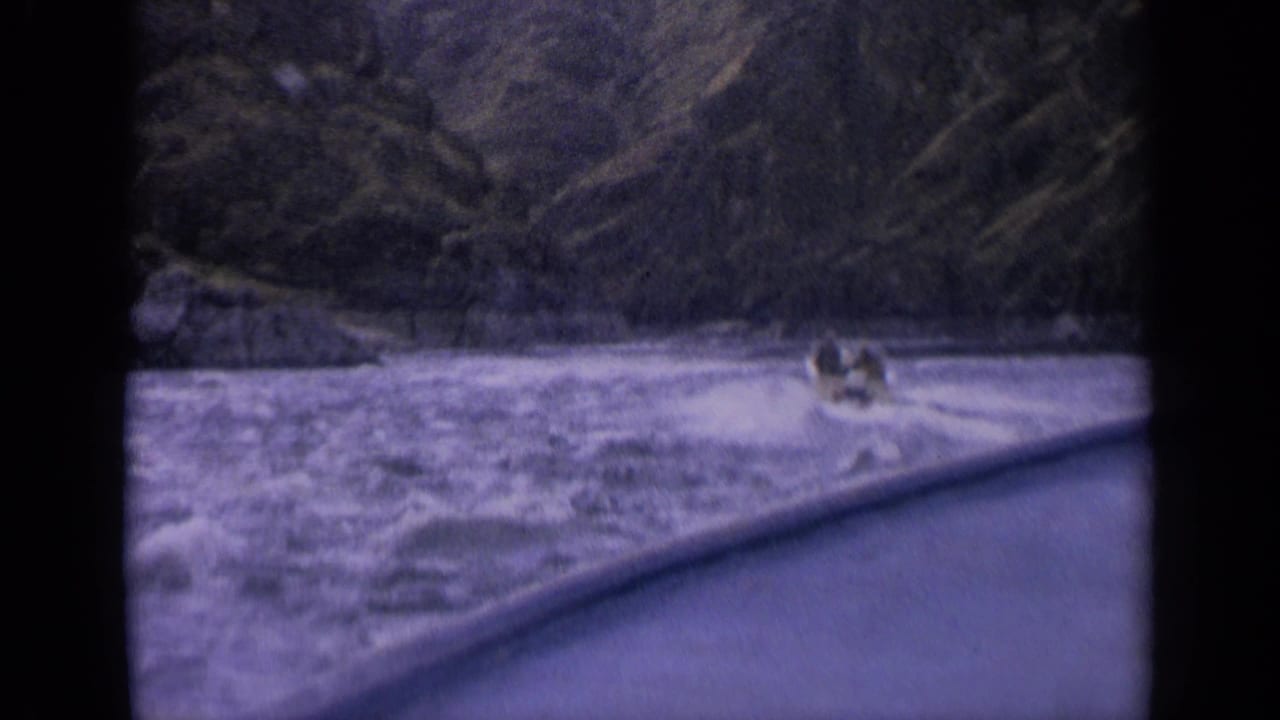 Small boat crossing rough river water beneath steep forested banks.