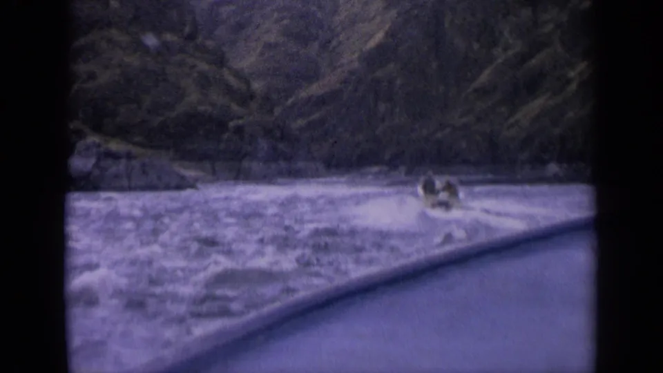 1963 Idaho 8mm frame showing a small boat with people aboard moving through churning mountain river water.