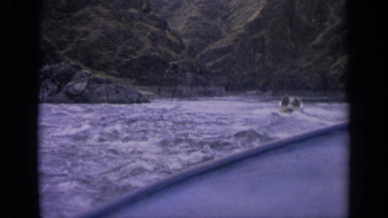 Boat farther across turbulent water near rocky riverbank.