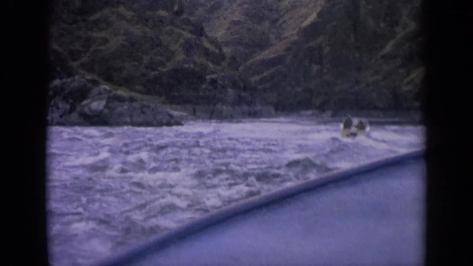 Small boat with visible occupants moves through turbulent Idaho river water in a purple-shifted 8mm home-movie frame.