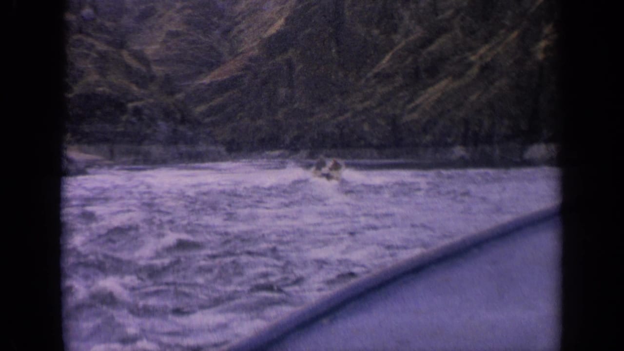 Small occupied boat continues through rough Idaho mountain river water, framed by dark 8mm borders and purple color shift.