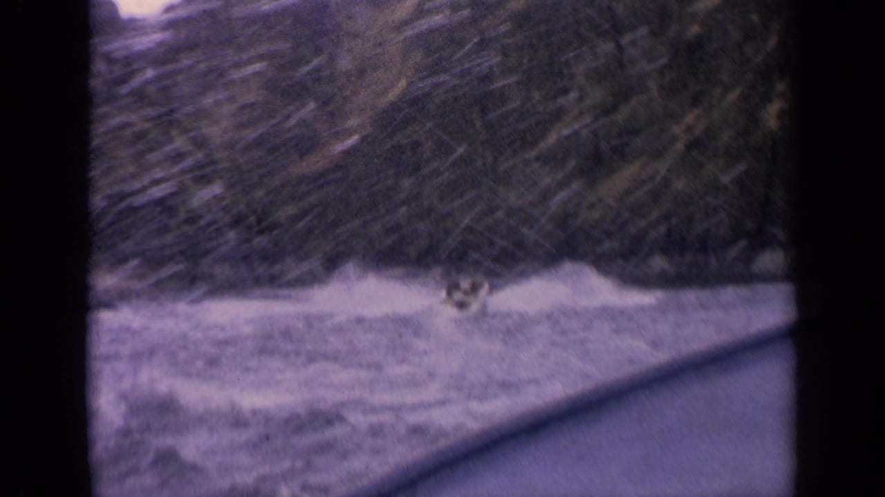 Small speedboat making white spray on a lake below wooded rocky hills.