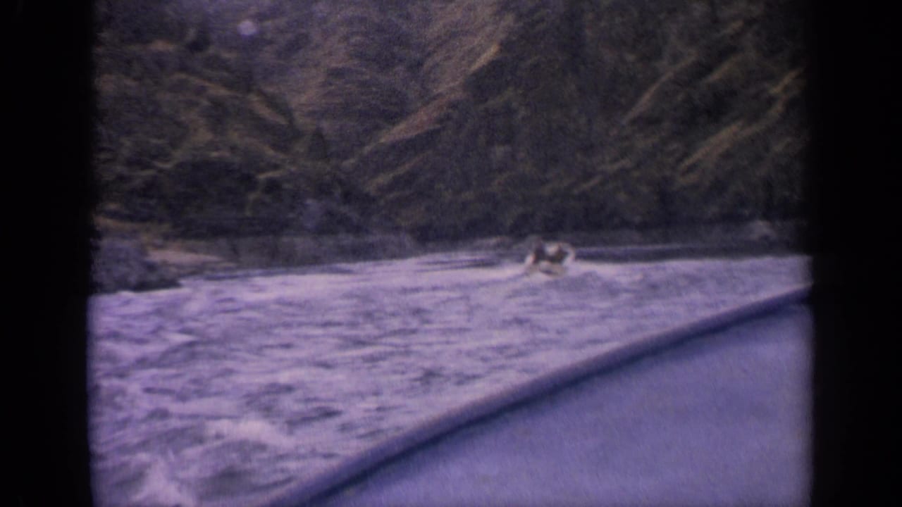 1963 Idaho home-movie frame showing a distant speedboat and foamy wake on a mountain lake.