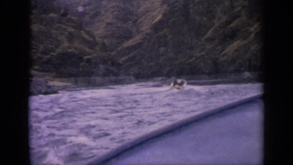 1963 Idaho home-movie frame showing a distant speedboat and foamy wake on a mountain lake.