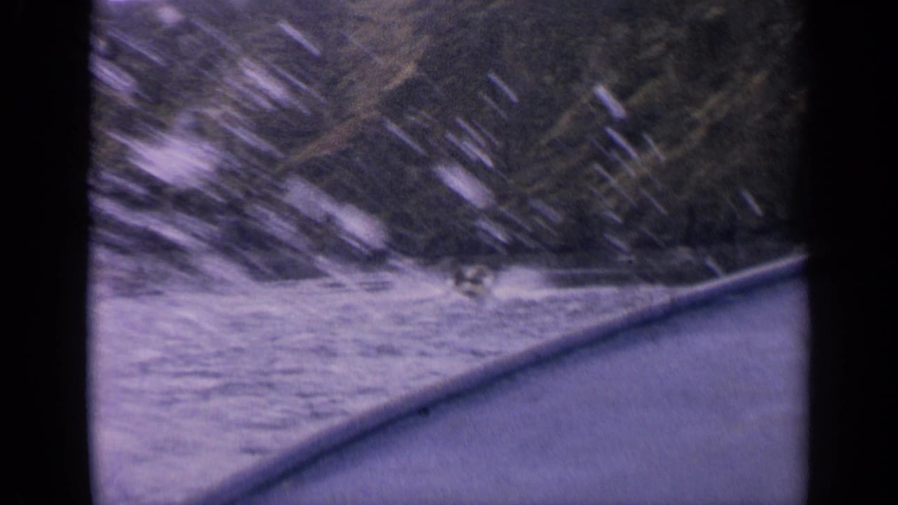 8mm frame from 1963 Idaho showing a speedboat partly hidden by spray on a lake beneath forested hills.