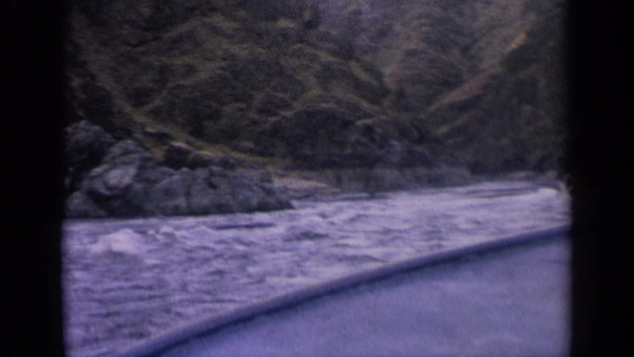 1963 Idaho lake view from a moving boat, showing water, rocky shore, and steep wooded hills.