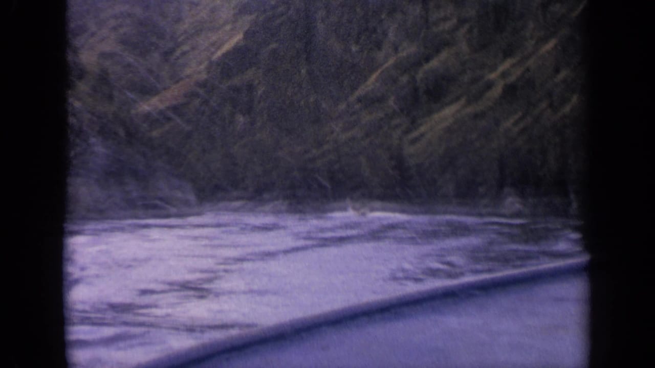 Canoe bow entering fast river water beside a dark forested bank.