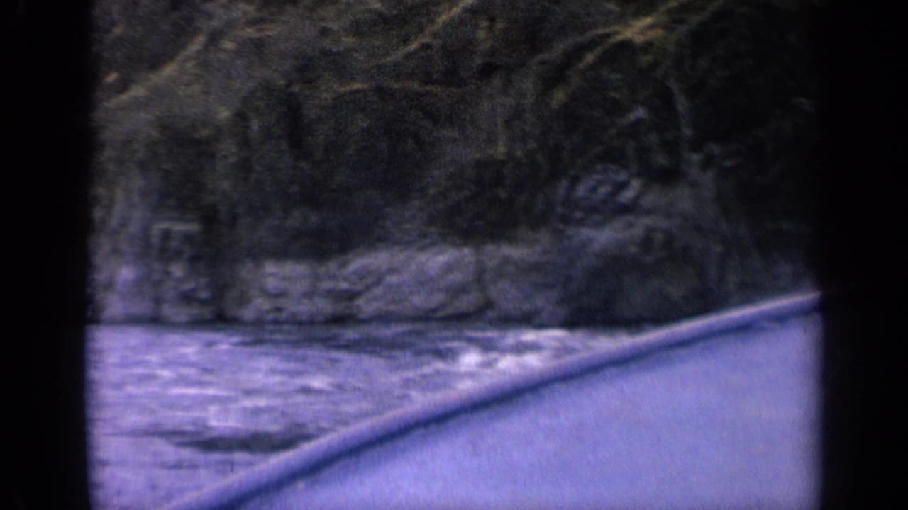 1963 Idaho river footage with the canoe bow cutting past foaming rapids and a rugged wooded shoreline.
