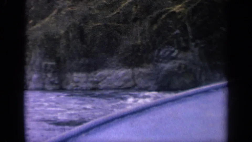 1963 Idaho river footage with the canoe bow cutting past foaming rapids and a rugged wooded shoreline.