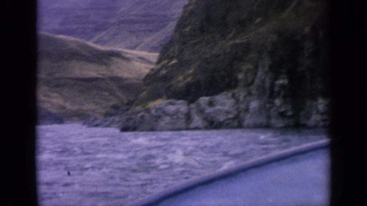 1963 Idaho river-canyon view from a boat, with rough water, rock faces and dry slopes beyond.