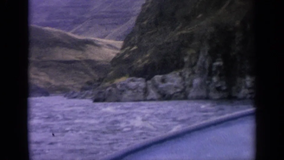 1963 Idaho river-canyon view from a boat, with rough water, rock faces and dry slopes beyond.