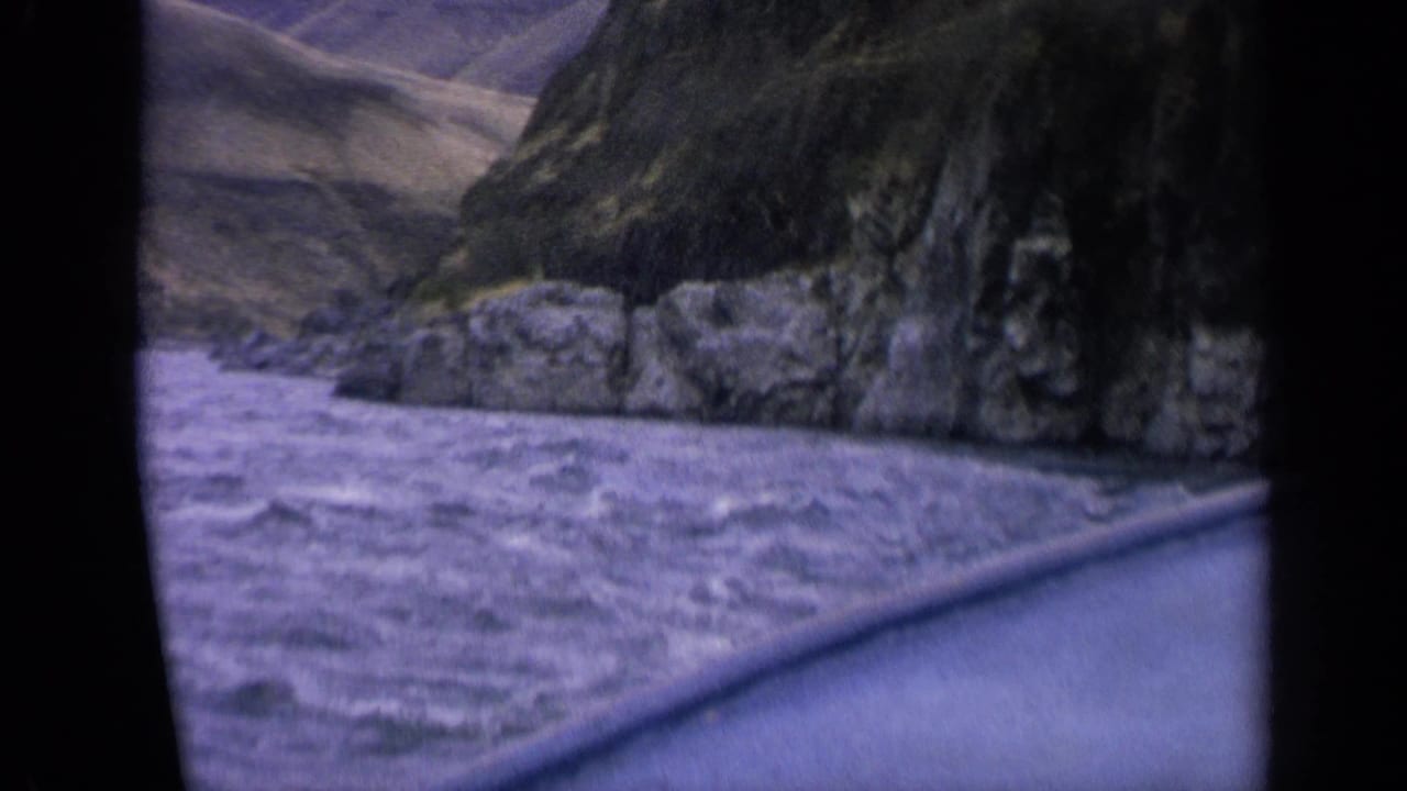 Vintage 8mm Idaho boat-view frame with foaming river water, canyon rocks and muted purple film color.