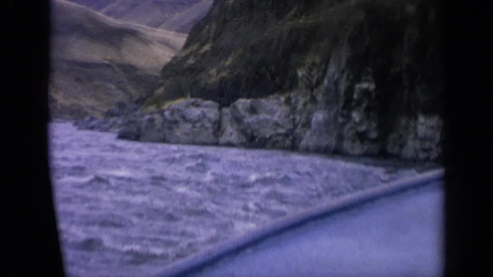 Vintage 8mm Idaho boat-view frame with foaming river water, canyon rocks and muted purple film color.