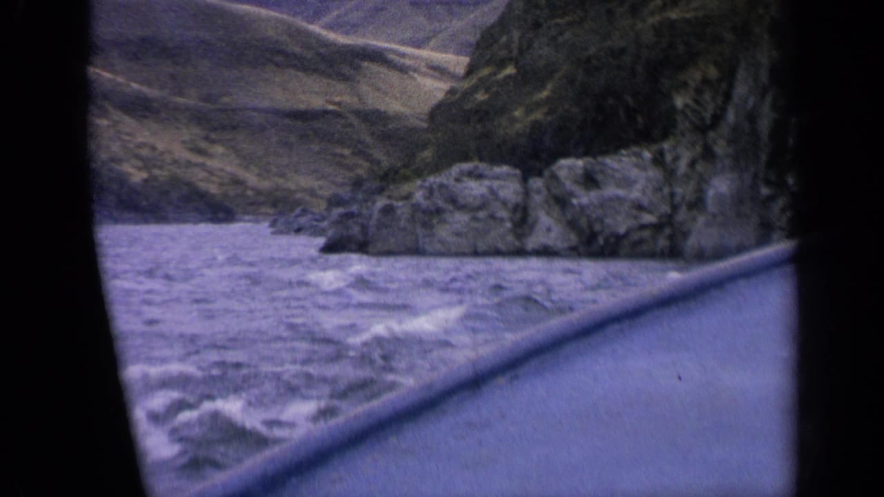 1963 Idaho home-movie frame showing river rapids, a boat edge and rocky canyon terrain under soft 8mm grain.