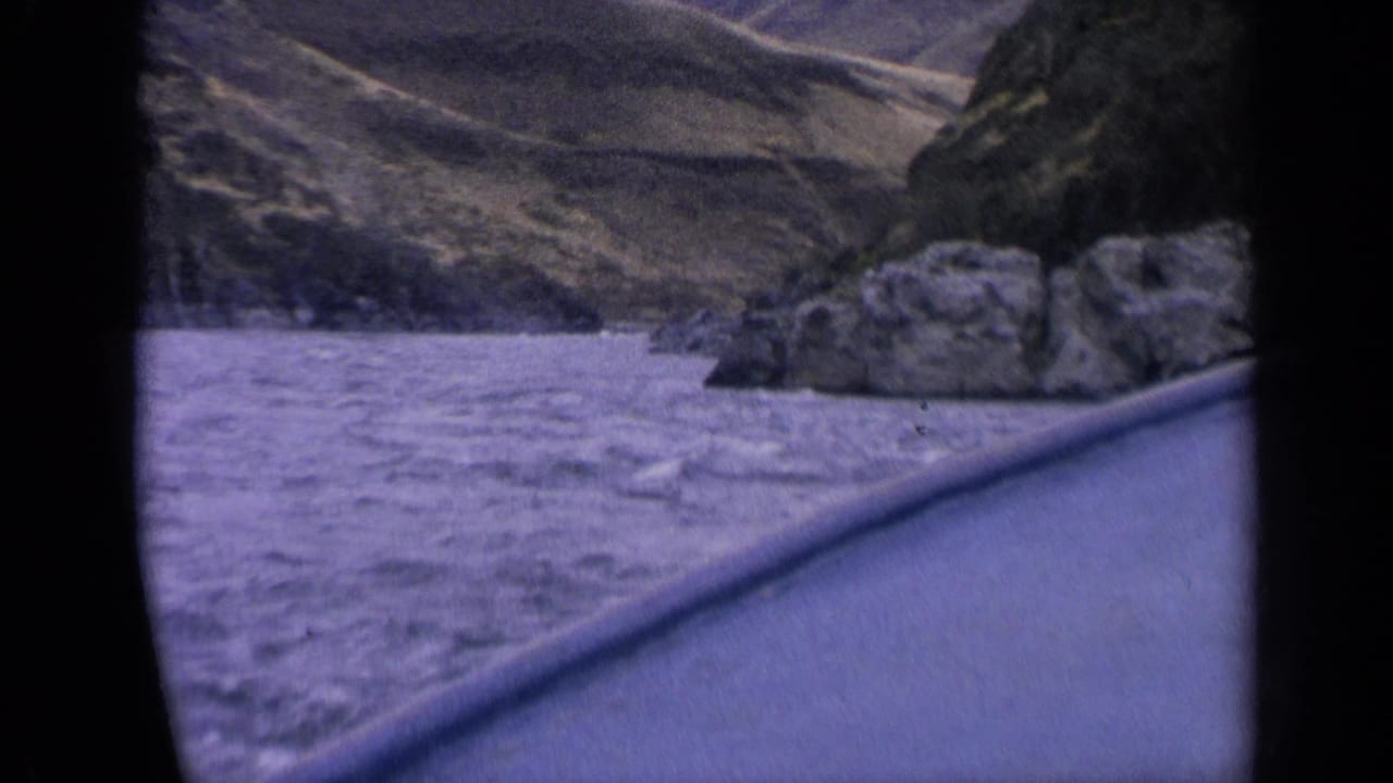 Roadside view of a river below rocky hills from a moving vehicle.