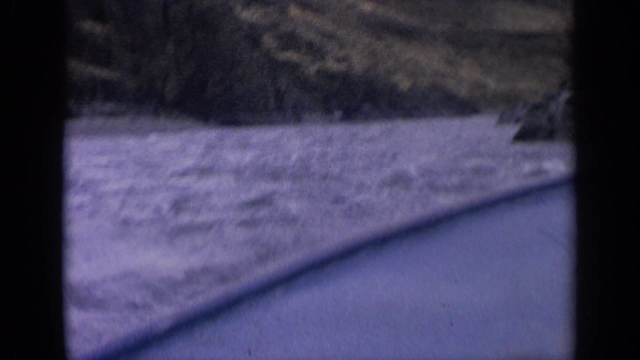 Motion-softened 1963 Idaho road-trip frame with river water, hillside shadows, and a diagonal roadside edge.