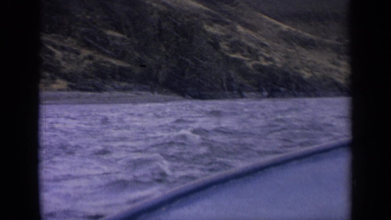 Choppy river beside a rocky, tree-covered hillside, partly framed by dark film borders.