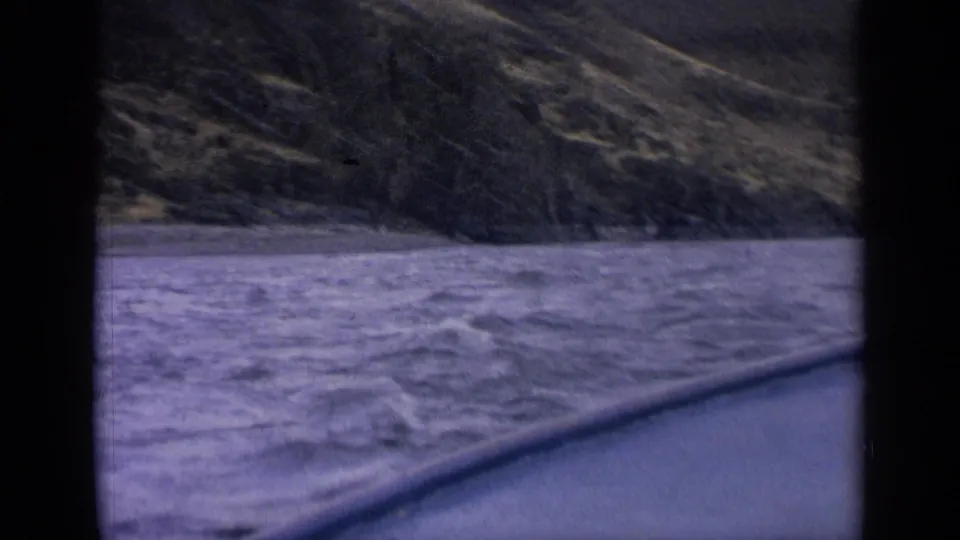 1963 Idaho 8mm view of a fast river and wooded hillside seen through dark frame edges during travel.