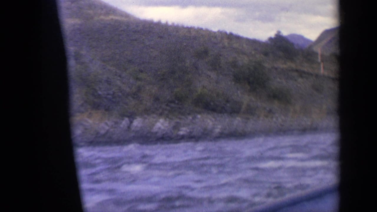 1963 Idaho home-movie view of rippled river water, rocky shoreline, wooded slopes, and distant hills.