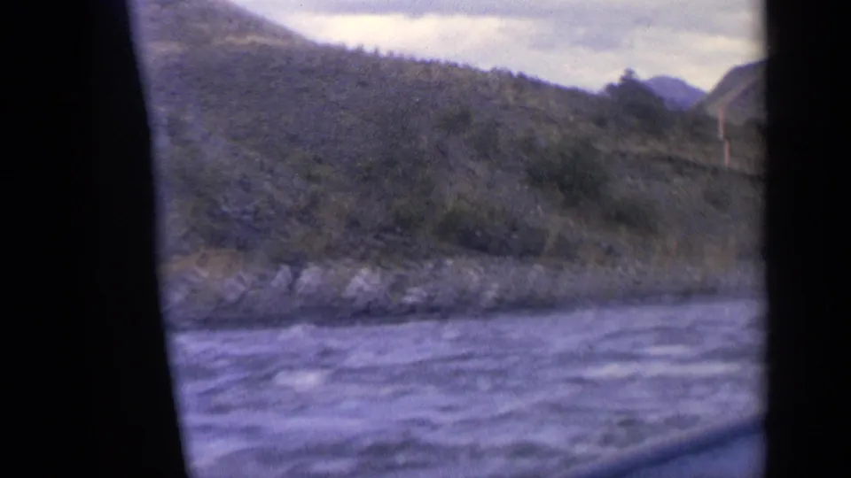1963 Idaho home-movie view of rippled river water, rocky shoreline, wooded slopes, and distant hills.