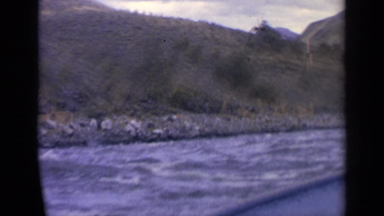 Choppy river water seen from a boat with rocky bank and low hills beyond.