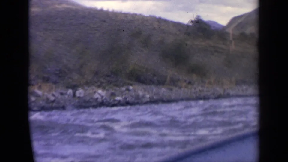1963 Idaho 8mm frame showing a moving boat view across choppy river water toward rocky banks and muted hills.