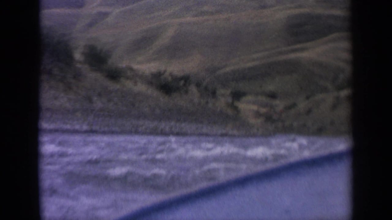 Choppy river water seen from a boat with green hills beyond the shoreline.